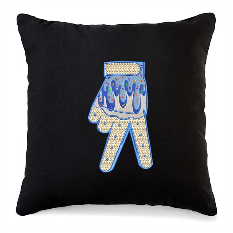 May include: A black pillow with a blue and white embroidered hand with sprinkles on top. The hand is making the peace sign.