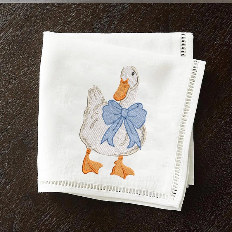 May include: White embroidered kitchen towel with a blue bow and a white duck with an orange beak.