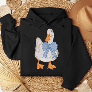 May include: Black hooded sweatshirt with a white duck wearing a blue bow tie embroidered on the front.