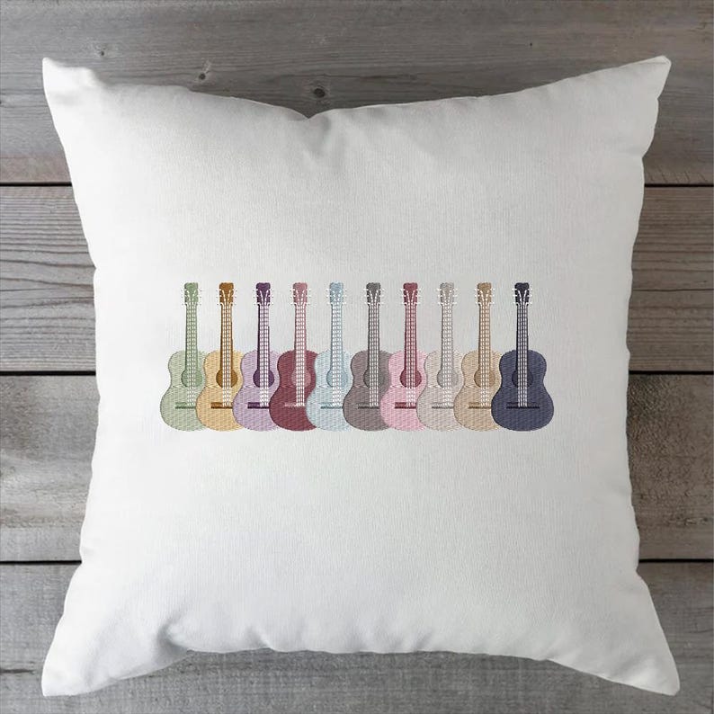 May include: White square pillow featuring an embroidered design of ten colorful guitars. The guitars are arranged in a row, each with a different pastel color, including green, yellow, purple, and blue. The pillow is made of a soft, white fabric.