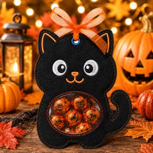 May include: A black felt cat-shaped treat bag featuring embroidered white eyes, an orange nose, and a mouth. The center has a circular clear window filled with orange foil-wrapped chocolates. An orange ribbon bow is tied at the top of the cat.