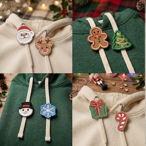 May include: A collection of four hoodies in cream and dark green, each featuring two decorative holiday-themed patches attached to the drawstring cords. The patches include a Santa, reindeer, gingerbread person, Christmas tree, snowman, snowflake, gift, and candy cane.