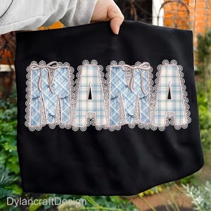 May include: Black tote bag with the word "MAMA" in large, decorative letters. The letters are blue plaid with pink bows and a white lace trim. The text "DylancraftDesign" is at the bottom.