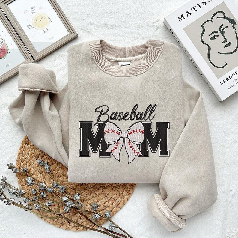 Peut inclure: Un sweat-shirt beige avec le texte "Baseball Mom" en lettres noires avec un n&oelig;ud de baseball rouge et blanc.
