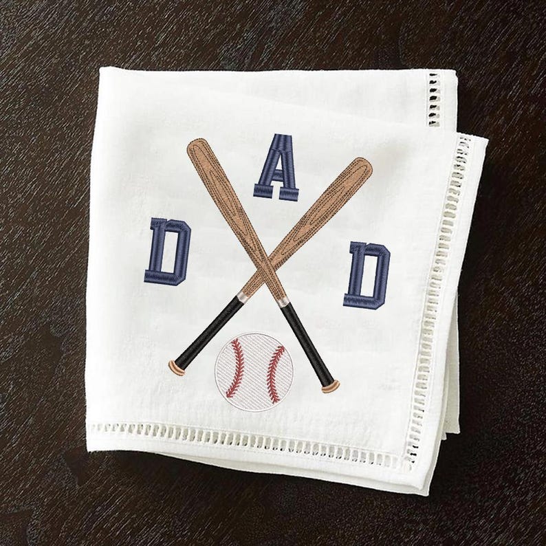 May include: White baseball-themed napkin with embroidered design. Features crossed baseball bats, a baseball, and the word "DAD" in navy blue letters. The napkin has a decorative, cut-out border.