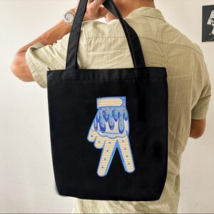 May include: Black tote bag with a blue and white peace sign design. The peace sign is decorated with colorful sprinkles.