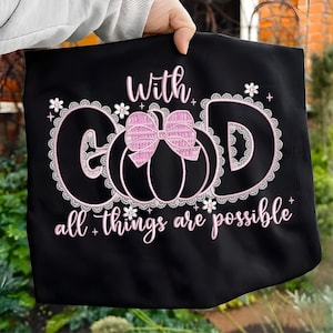 Può includere: Borsa tote nera con la scritta "With God all things are possible" in rosa. La parola "GOD" è disegnata con una zucca e un fiocco rosa e pizzo bianco.