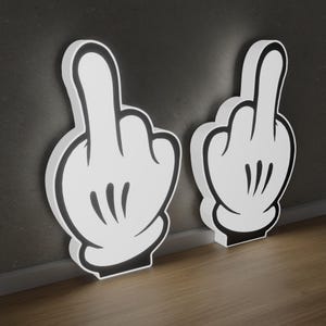 Pode incluir: Duas mãos brancas de estilo de desenho animado com detalhes pretos, cada uma mostrando o dedo do meio. As mãos são tridimensionais e parecem ser feitas de espuma ou plástico.