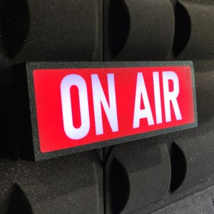 Peut inclure: Un panneau rectangulaire noir avec un fond rouge et du texte blanc qui dit "ON AIR".