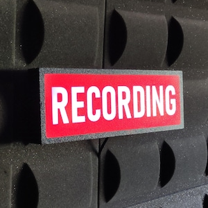 Peut inclure: Un panneau rouge avec du texte blanc qui indique "RECORDING" sur un fond noir.