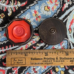 May include: An open, dark wooden box with a bright red wax seal inside. The seal has a design of a crescent moon and leaves. A wooden ruler with inch markings is in the foreground.