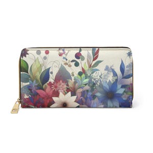 Op de afbeelding: Een portemonnee met bloemenprint en een gouden ritssluiting. De portemonnee heeft een crèmekleurige achtergrond met een aquarelontwerp van bloemen in tinten rood, blauw en groen. De ritstrekker is rechthoekig.