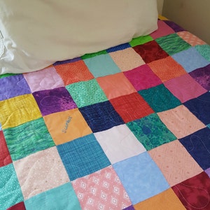 May include: A colorful patchwork quilt with a variety of fabrics and patterns. The quilt is made up of squares of different colors, including red, blue, green, yellow, and purple. The quilt is stitched together with a white thread. The quilt has the name "Scarlett" embroidered on one of the squares.