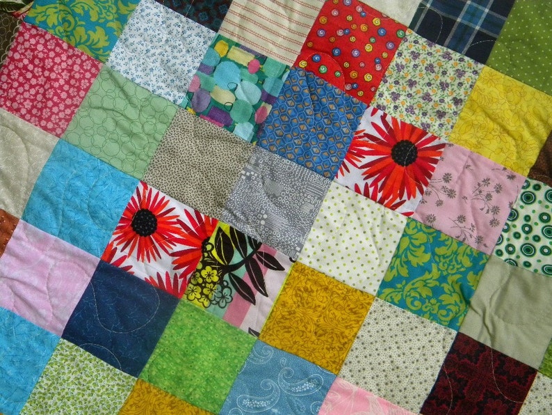 Puede incluir: Un edred&oacute;n de retazos con una variedad de cuadrados de tela coloridos. El edred&oacute;n presenta cuadrados en tonos de azul, verde, rosa, amarillo y rojo, con estampados florales y geom&eacute;tricos. El edred&oacute;n est&aacute; cosido a mano.