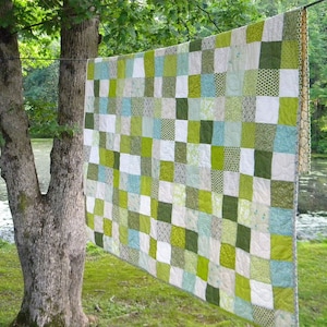 May include: A patchwork quilt with squares of green, blue, and white fabric. The quilt is hanging on a clothesline outside.