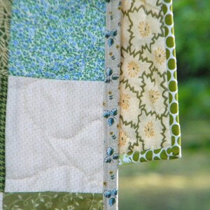 May include: A patchwork quilt with a variety of floral patterns in shades of green, blue, and white. The quilt is edged with a green and white polka dot trim.