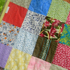 Puede incluir: Primer plano de un edred&oacute;n de patchwork con una variedad de cuadrados de tela coloridos. El edred&oacute;n presenta cuadrados en patrones rojos, azules, verdes, rosas y florales. Los bordes est&aacute;n adornados con un borde estampado.