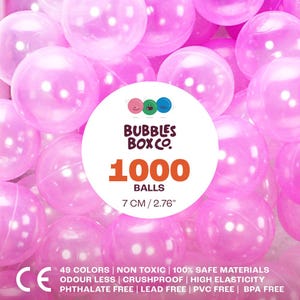 Op de afbeelding: Een verzameling doorschijnende roze speelballen. De afbeelding bevat een witte cirkelvormige afbeelding met de tekst "BUBBLES BOX CO." en "1000 BALLS". De ballen hebben een diameter van 7 cm. Extra tekst geeft aan dat de ballen niet giftig en veilig zijn.