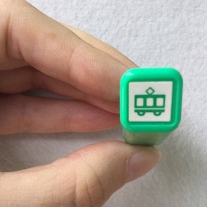 May include: A green stamp with a white image of a tram. The tram has a diamond-shaped roof and is outlined in black.