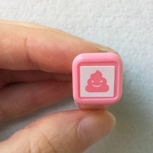 May include: A pink rubber stamp with a white poop emoji design.