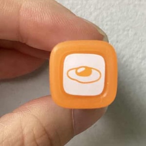 May include: A square orange marker cap featuring a white inset panel with a simple orange line drawing of a fried egg. The cap has rounded corners and a smooth plastic finish, displaying the icon clearly on the top surface of the marker end.