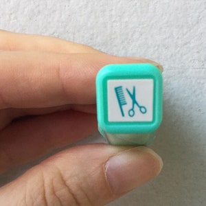 May include: A turquoise blue stamp with a white square and a black silhouette of a comb and scissors.