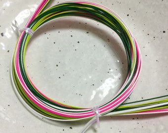 May include: A bundle of green, white, and pink string wrapped in a circle on a white plate with black speckles.