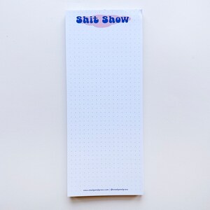 Könnte beinhalten: Weißer Notizblock mit blauem und rosafarbenem Text "Shit Show" oben. Der Notizblock hat ein gepunktetes Rastermuster und den Text "www.steelpetalpress.com | @steelpetalpress" unten.