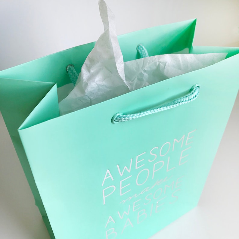 May include: A light green gift bag with white rope handles. The bag has the text "Awesome People" printed on the front in white.