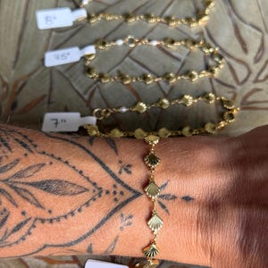 May include: Four gold-toned chain bracelets featuring repeating shell-shaped links and small white beads. Each bracelet has a white tag attached indicating lengths of 6.5 inches, 7 inches, 7.5 inches, and 8 inches respectively.