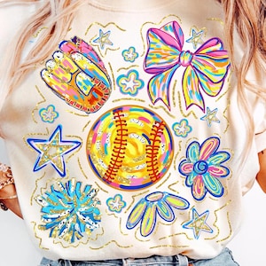 May include: Cream-colored t-shirt featuring a colorful baseball-themed design. The design includes a baseball, a glove, a bow, stars, and flowers. The graphics are outlined in gold and have a watercolor effect.