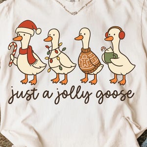 May include: Cream-colored t-shirt with a whimsical design featuring four cartoon geese dressed in festive attire. The geese are adorned with a Santa hat, Christmas lights, a sweater, and earmuffs. The text "just a jolly goose" is written below the geese.