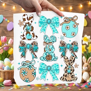 May include: A white sheet featuring Easter-themed designs. The designs include cartoon bunnies, bows, and Easter eggs in brown, turquoise, and leopard print patterns. The sheet is held up by a hand, with a wooden background.