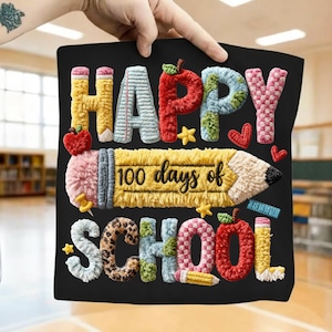 May include: Black square sign with colorful embroidered text and images. The text reads "HAPPY SCHOOL" with a pencil that says "100 days of". The design includes apples, stars, and hearts.