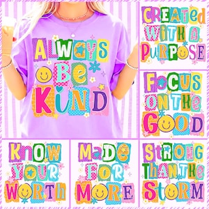 May include: A lilac-colored t-shirt with the words "ALWAYS BE KIND" in colorful, block letters. The design includes smiley faces, stars, and flowers. Additional graphics with positive messages are also displayed.