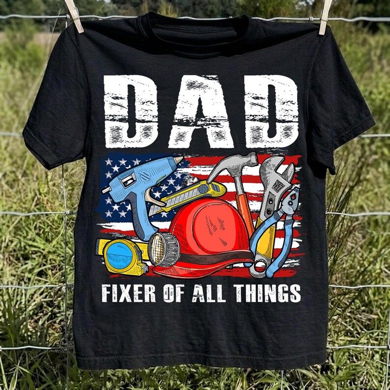 May include: Black t-shirt with the word "DAD" in white block letters above a graphic of tools and a red, white, and blue American flag. The text "FIXER OF ALL THINGS" is below the graphic.