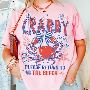 May include: Pink t-shirt with a crab graphic in red and blue, and the text "If Crabby, Please Return to the Beach." The design includes a seashell, starfish, and the words "sun, salt, sass, feeling beachy."