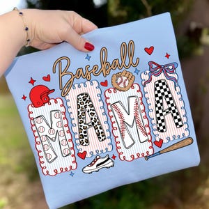 Könnte beinhalten: Hellblaues T-Shirt mit dem Wort "Baseball Mama" in einer dekorativen Schriftart. Die Buchstaben "MAMA" sind mit Baseball-Mustern gefüllt, darunter Basebälle, Leopardenmuster und ein Schachbrettmuster. Baseball-bezogene Grafiken sind ebenfalls enthalten.