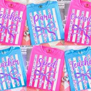 Puede incluir: Una colección de camisetas rosas y azules con diferentes títulos de trabajo impresos, incluyendo "Teacher", "Para", "Counselor" y "Sped". Cada camiseta presenta un diseño a rayas con un lazo y estrellas.