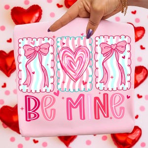 May include: A pink Valentine's Day themed graphic with the words "Be Mine". The design includes three framed illustrations of a heart and bows with ribbons. The background features red heart-shaped balloons and small hearts.