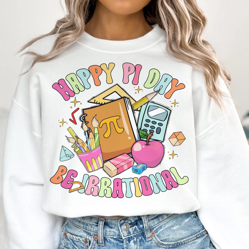 May include: White sweatshirt with a colorful graphic design that says "Happy Pi Day Be Irrational". The graphic includes a notebook, pencils, a calculator, a protractor, a ruler, an apple, and a pi symbol.