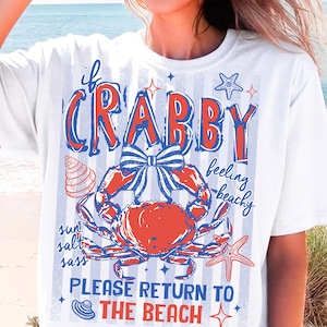 May include: White t-shirt with a red and blue crab graphic and the words "If Crabby Feeling Beachy Please Return to the Beach". The design includes a crab, starfish, and seashell.
