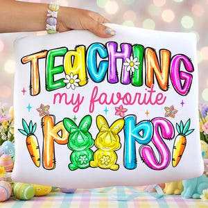 May include: White pillow with the text "TEACHING my favorite PEEPS" in colorful bubble letters. The design includes daisies, carrots, and Easter bunny illustrations. The pillow is held by a hand wearing a bunny bracelet.