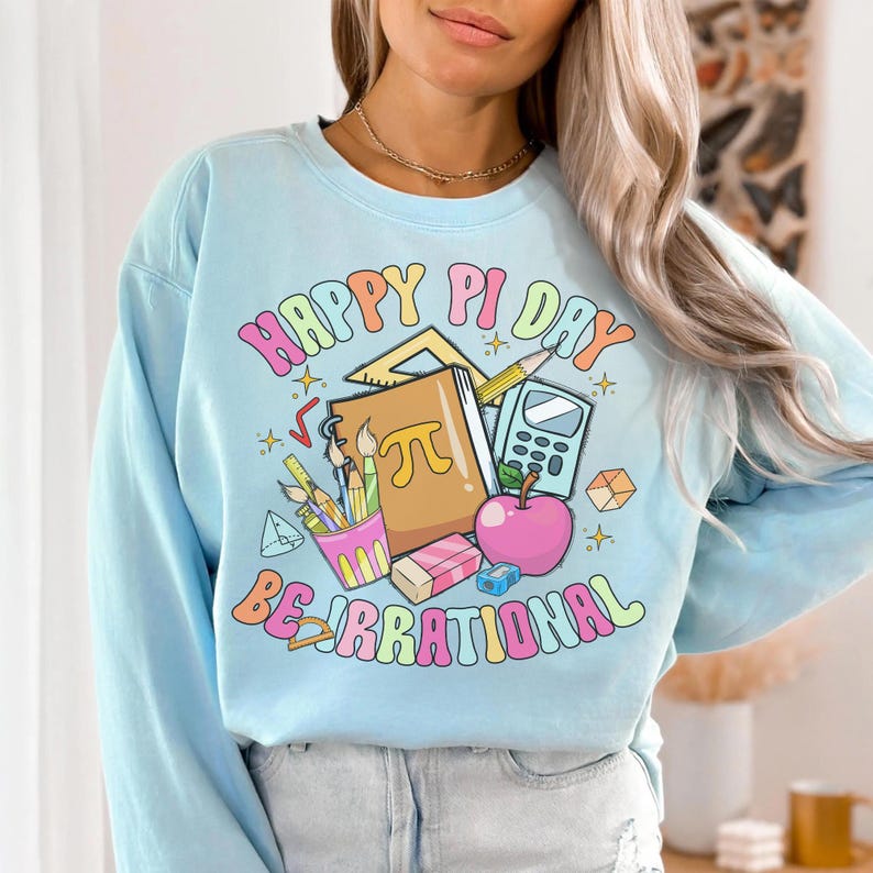 May include: Light blue sweatshirt with a graphic print of school supplies and the text "Happy Pi Day Be Irrational".