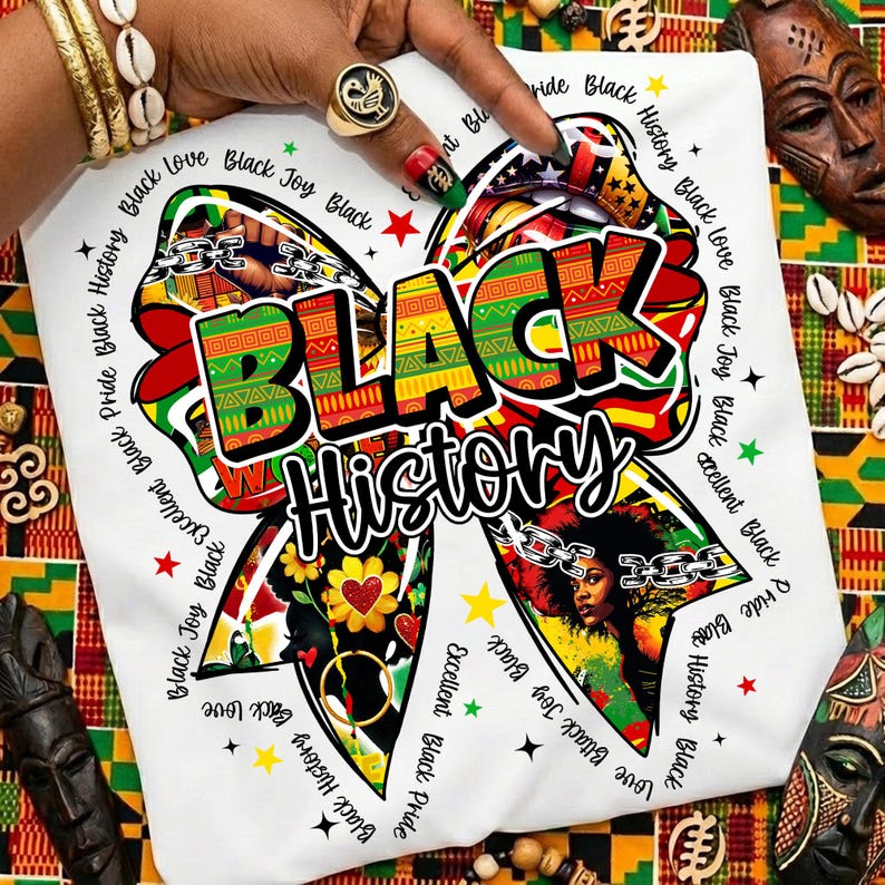 May include: White t-shirt with a colorful bow design featuring the words "BLACK History." The bow incorporates red, green, yellow, and black patterns, with additional text around the bow. The shirt is held by a hand with gold jewelry and a ring.