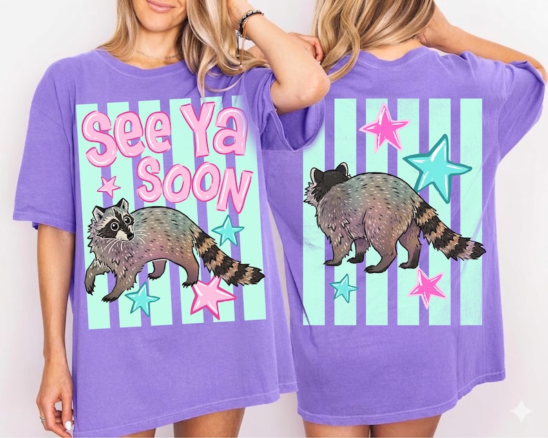 May include: A purple t-shirt with a raccoon graphic and the text "See Ya Soon". The design includes pink and teal stars and vertical stripes. The raccoon has a gray and brown body with a striped tail.