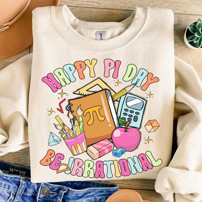 May include: A light beige sweatshirt with the text "Happy Pi Day Be Irrational" in rainbow colors. The text is surrounded by a variety of school supplies, including a calculator, pencils, a ruler, an eraser, and a notebook with the symbol for pi.