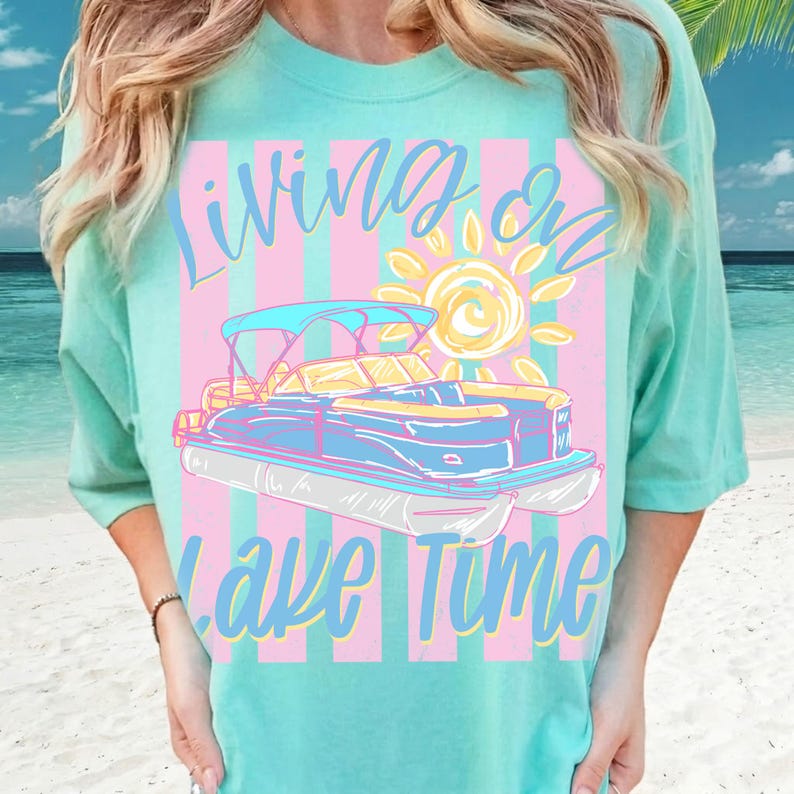May include: A light teal t-shirt with a graphic of a pontoon boat, sun, and text that reads "Living on Lake Time." The design features a blue and yellow boat with a pink and blue striped background.