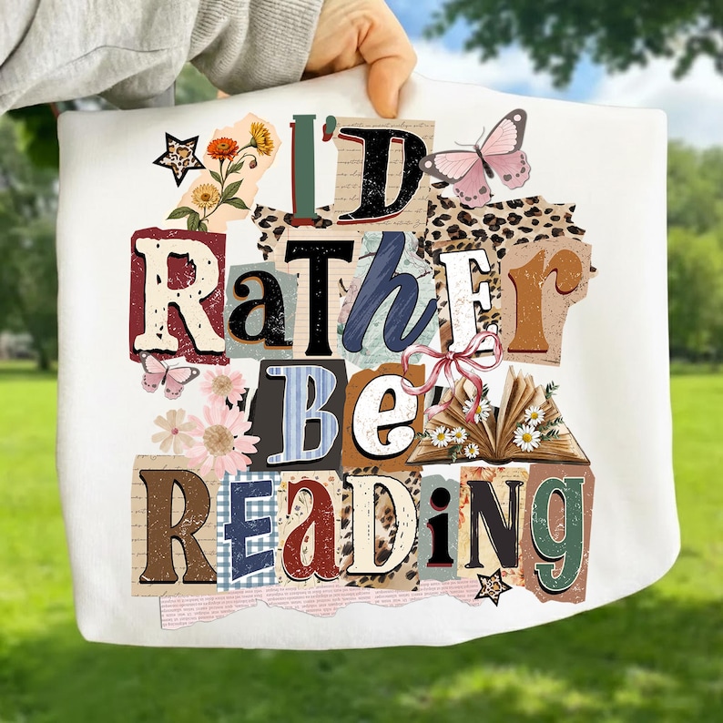 May include: White tote bag with the text "I'd Rather Be Reading" in a collage style. The design includes butterflies, flowers, and an open book. The letters are in various colors and fonts.
