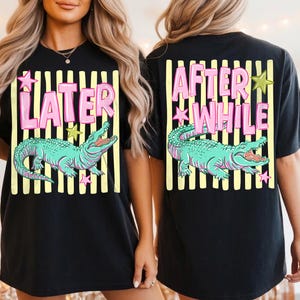 May include: Black t-shirt featuring a teal alligator graphic with the words "LATER" and "AFTER WHILE" in pink. The design includes yellow stripes and star accents, creating a playful and eye-catching design. A casual, unisex tee.